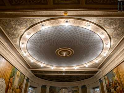 Al di sotto di un soffitto riccamente decorato con motivi vegetali grigi e dorati...